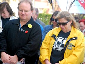 Two workers bow their heads during an Ontario Day of Mourning ceremony