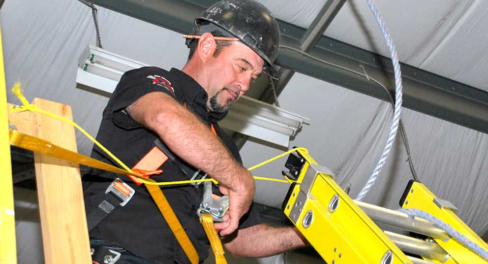 A man with a hardhat works on top of a ladder.