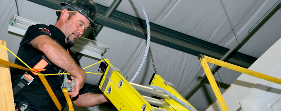 A man with a hardhat works on top of a ladder.