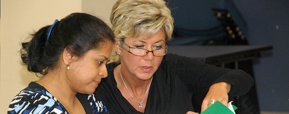 A woman with glasses teaches another woman at WHSC Training session.