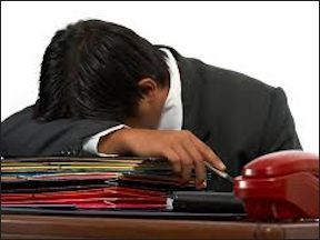 Stressed worker with head down on pile of documents