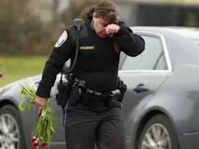 Police officer holding flowers and crying at a graveyard